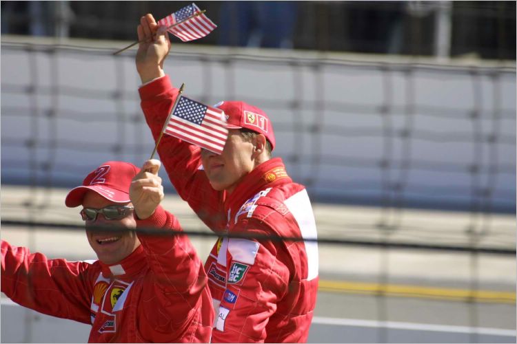 Rubens Barrichello to the left and Michael Schumacher to the right proudly wave the American flag.